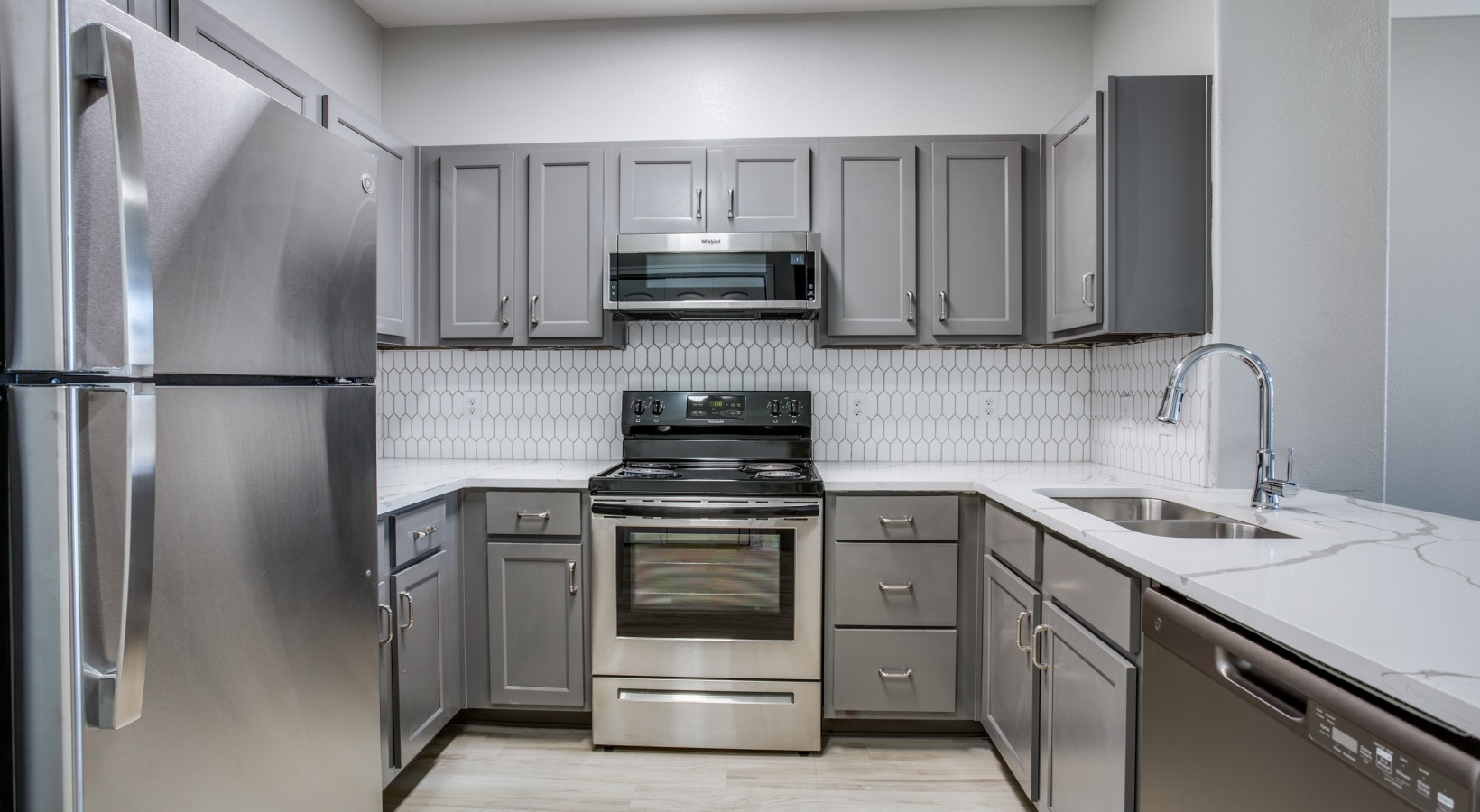 a kitchen with stainless steel appliances and gray cabinets at The  Franklin at Samuels Ave