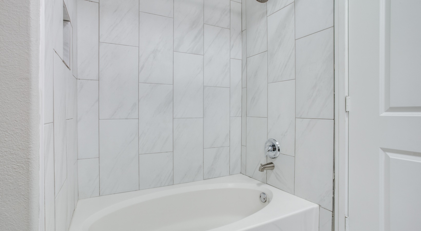 a bathroom with a tub and white tile walls at The  Franklin at Samuels Ave