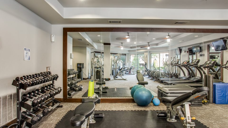 a gym room with exercise equipment and mirrors at The Franklin at Samuels Ave