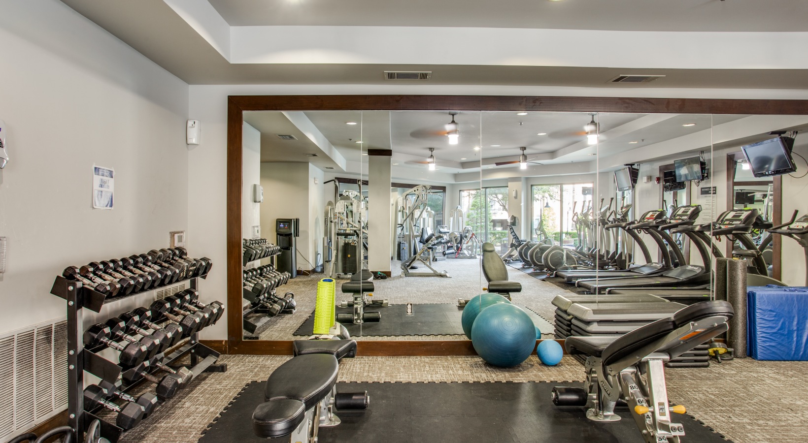 a gym room with exercise equipment and mirrors at The Franklin at Samuels Ave